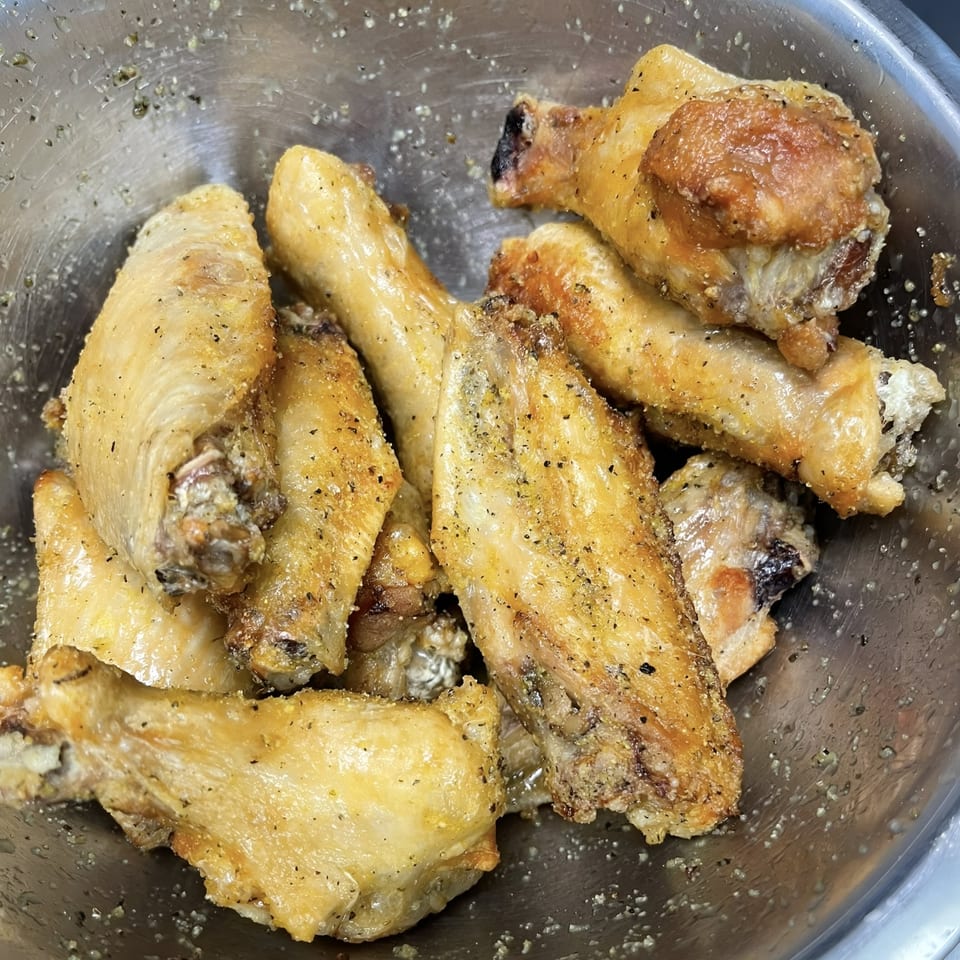Seasoned chicken wings and drumettes in a metal bowl, ready for cooking at Caffé OPA.