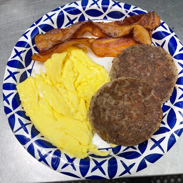 A breakfast plate with scrambled eggs, crispy bacon, and two sausage patties on a blue and white paper plate.