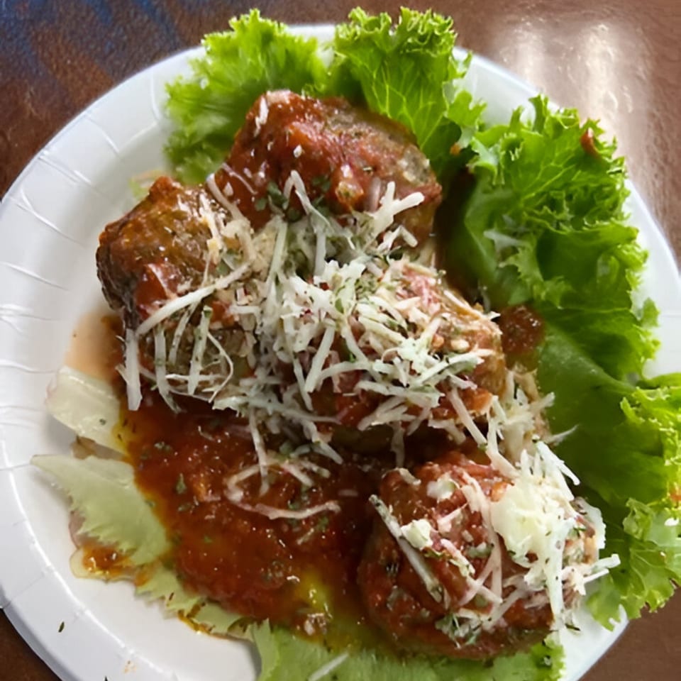 Greek meatballs with tomato sauce, shredded cheese, and fresh lettuce on a white plate.