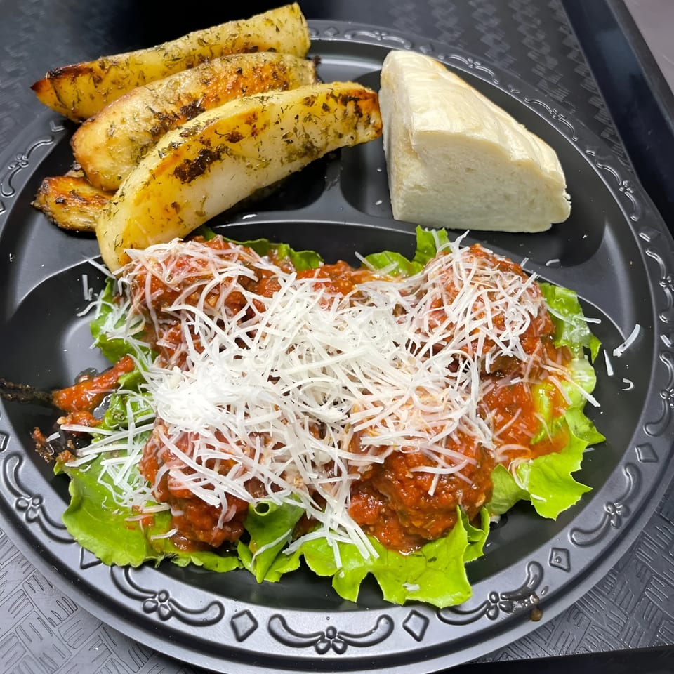 Greek meatballs with tomato sauce and shredded cheese, served with potato wedges and bread.