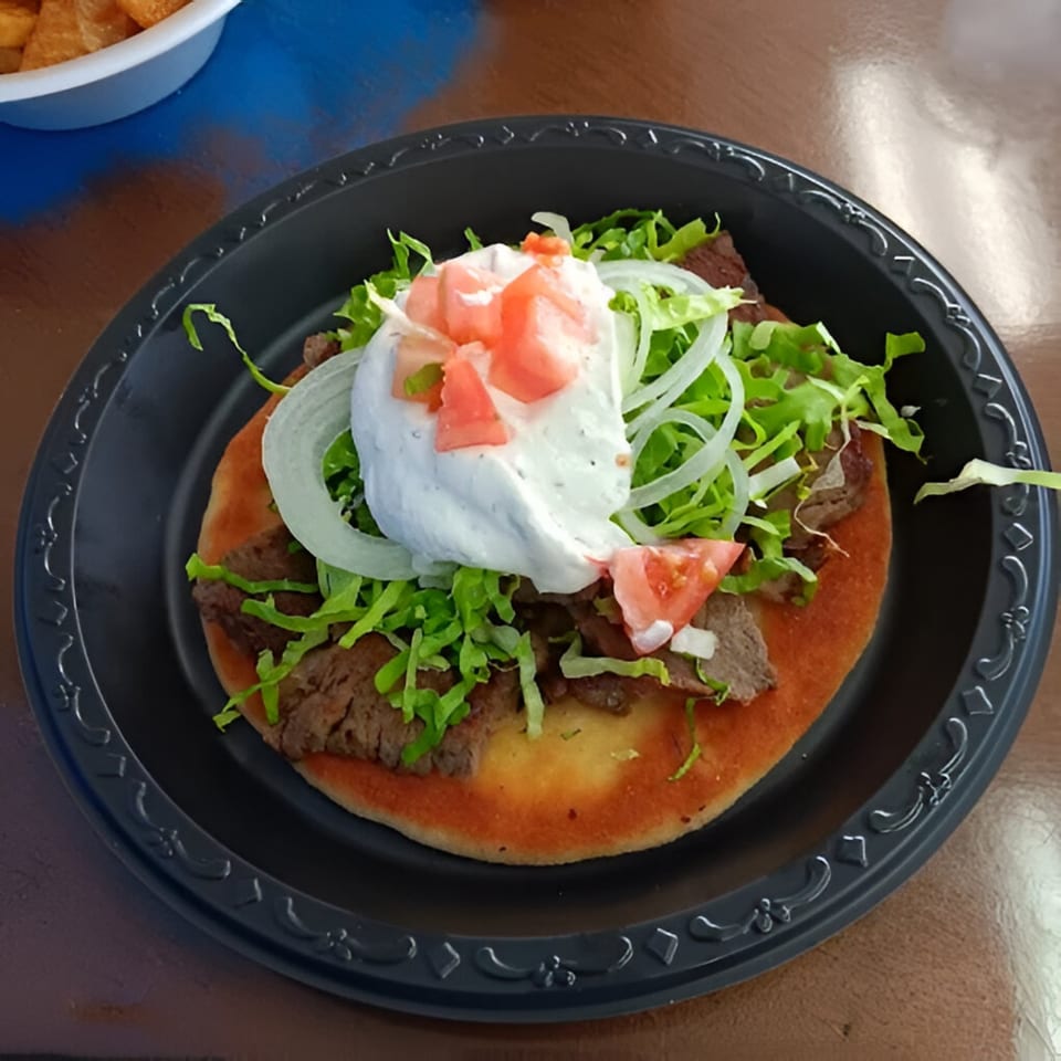 Greek gyro on pita bread with meat, lettuce, onions, tomatoes, and tzatziki sauce.