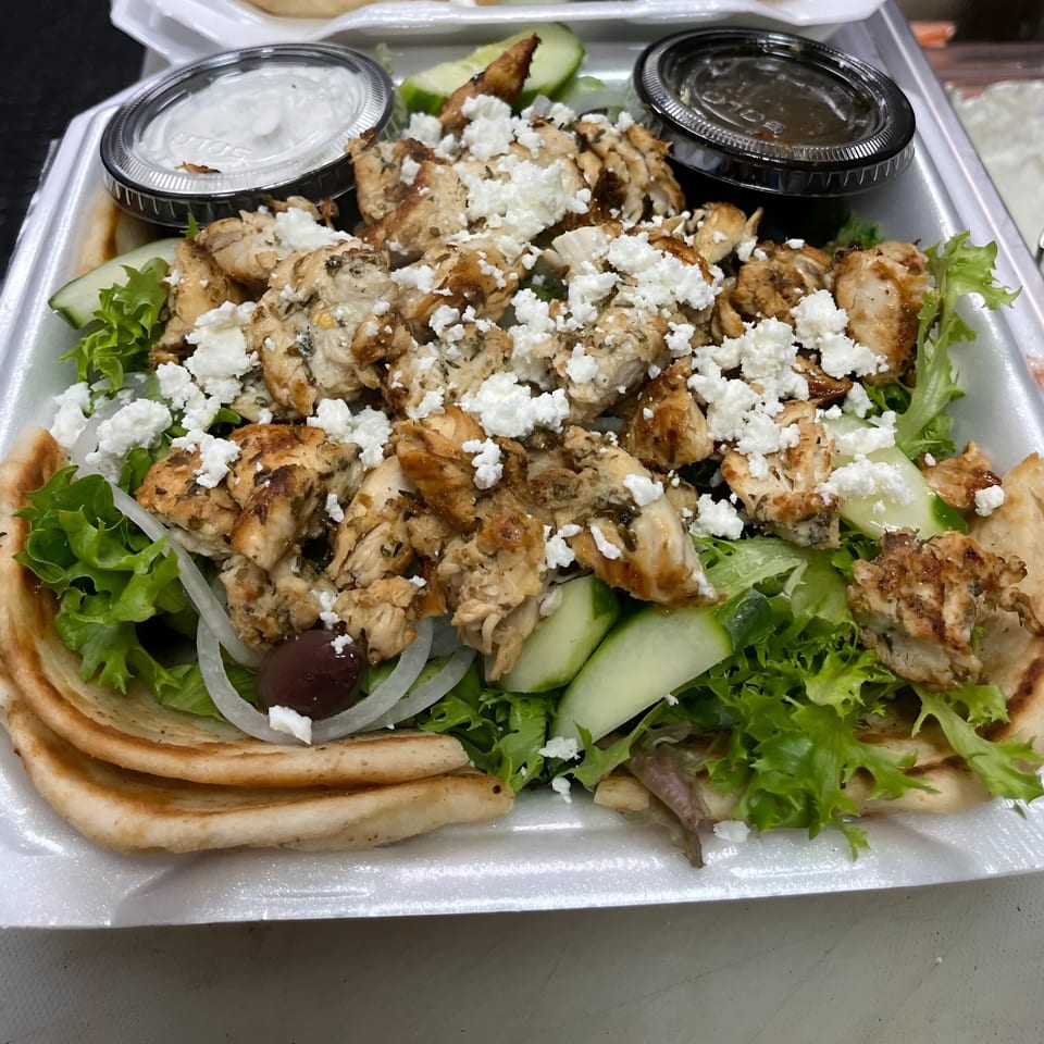 Greek chicken gyro platter with feta, lettuce, onions, cucumbers, olives, and pita bread.