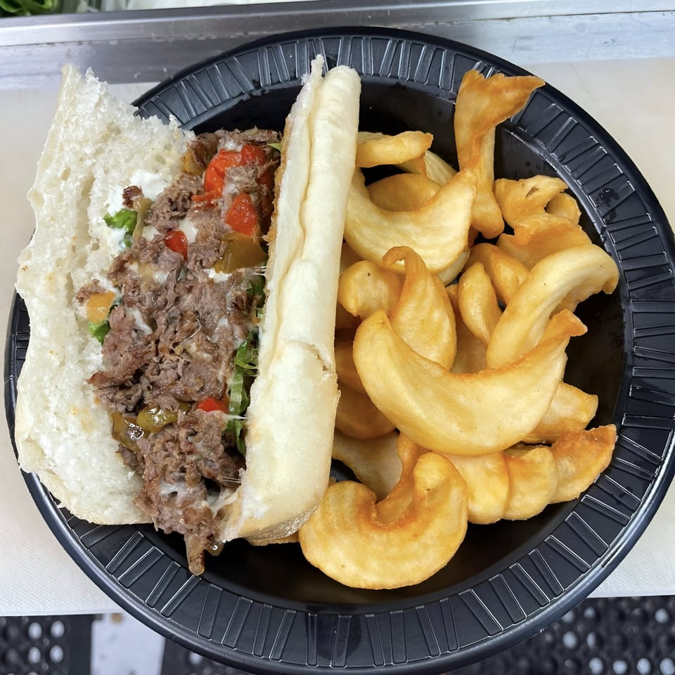 Caffé OPA's cheesesteak sandwich with peppers and onions, served with curly fries on a black plate.